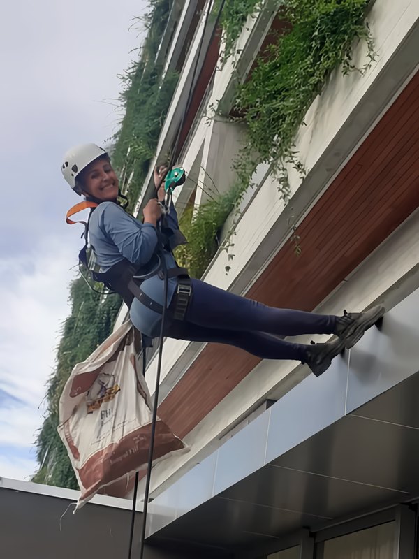 Colaboradora da Dubai Garden Rapel descendo por corda na fachada de um prédio com jardim vertical