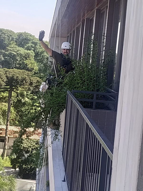 Colaborador da Dubai Garden Rapel suspenso por corda fazendo manutenção de floreira na fachada de um edifício