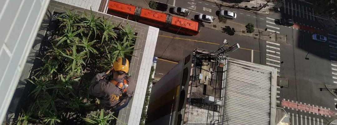 Profissional com capacete fazendo manutenção de canteiro em altura por acesso por corda
